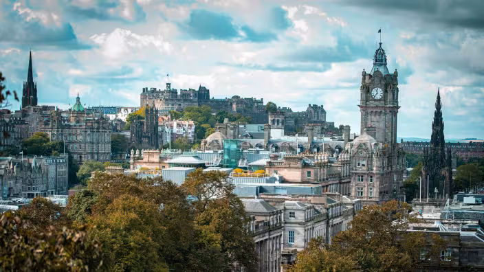 A panoramic landscape of downtown Edinburgh showcasing the city's iconic heritage buildings and urban green spaces.