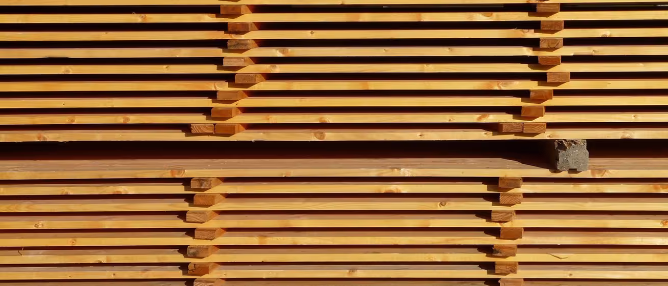 Stacks of evenly spaced, horizontal wooden planks drying in neat, symmetrical rows at a lumber yard.