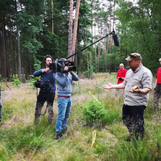 A forestry expert gives an interview to a film crew in a forest setting.