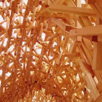 Intricate, overlapping light-colored wooden beams forming a dense, woven architectural ceiling structure.